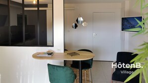 A modern living room with a dining area, a TV mounted on the wall, and a door leading to another room. - Town Hall Studio - Hyper-center Limoges (Limoges)