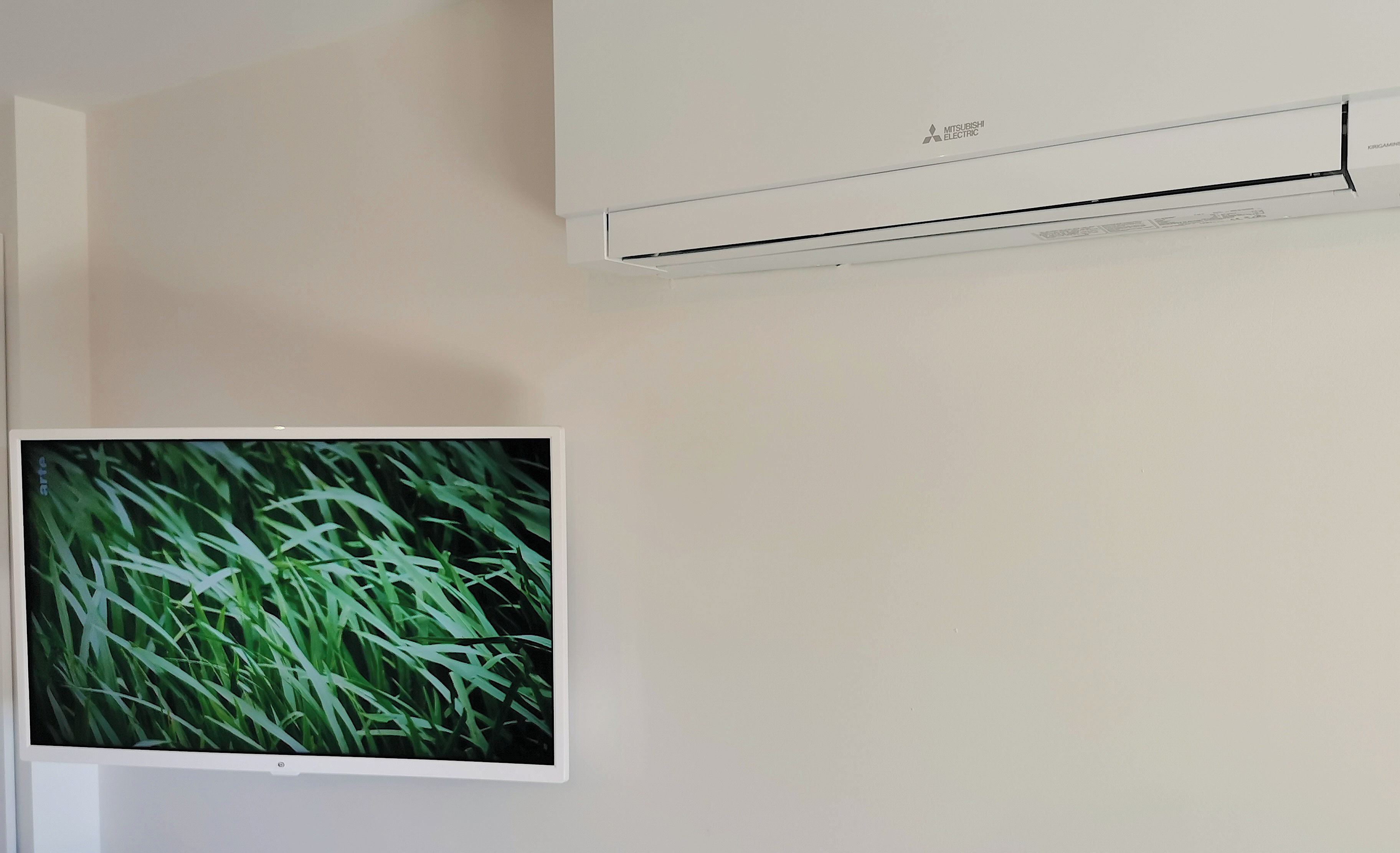 En vægmonteret klimaanlæg og et fladskærms-tv, der viser en græsplæne.