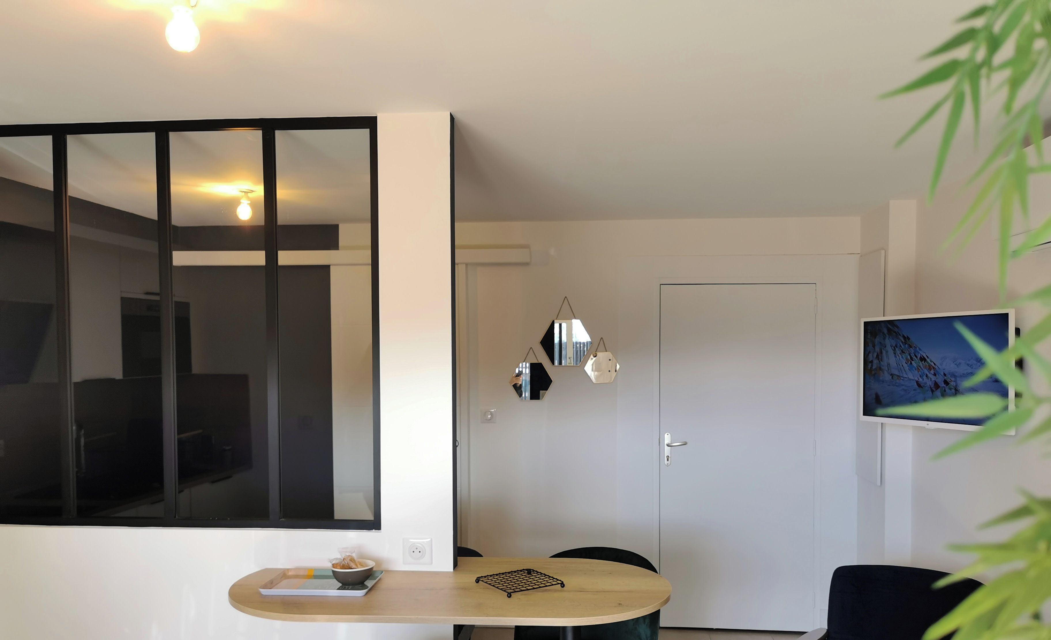 Een moderne woonkamer met een eetgedeelte, een aan de muur bevestigde televisie en een deur naar een andere kamer.