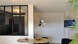 A modern living room with a dining area, a TV mounted on the wall, and a door leading to another room. - Town Hall Studio - Hyper-center Limoges (Limoges)