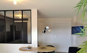 A modern living room with a dining area, a TV mounted on the wall, and a door leading to another room. - Town Hall Studio - Hyper-center Limoges (Limoges)