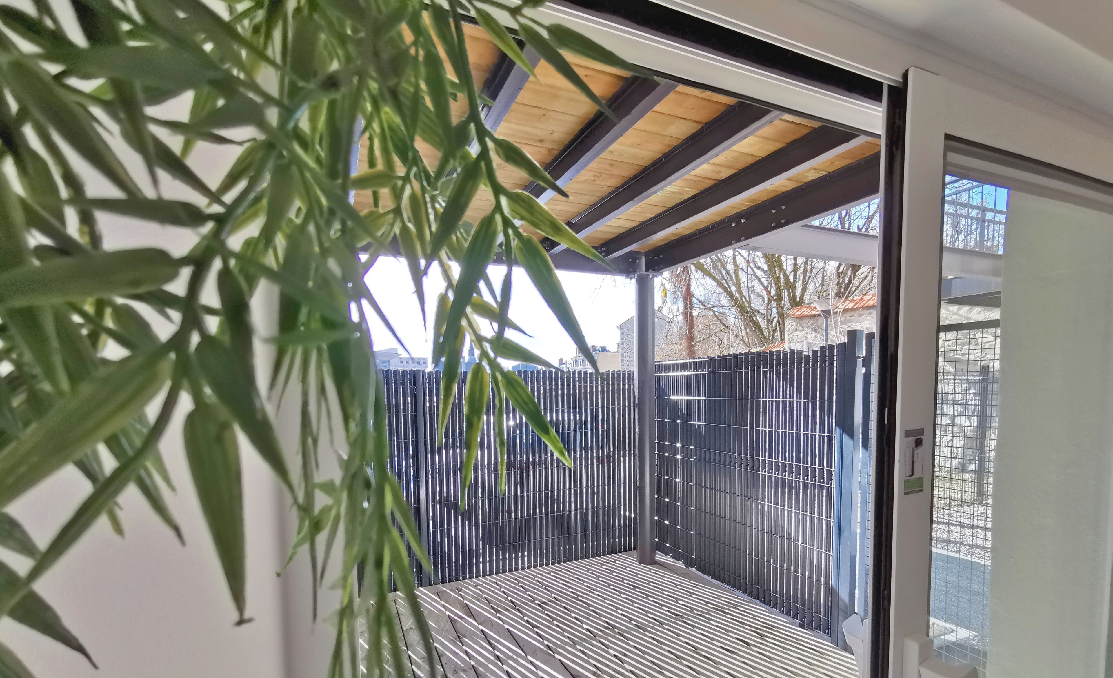 Un espace extérieur moderne et abrité, doté d’un plafond en bois et d’une rambarde en métal, offrant une vue sur les environs.
