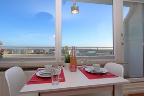 Ein Essbereich mit Tisch für zwei Personen, einer Champagnerflasche und Blick auf die Stadt durch große Fenster.