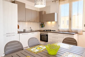 A modern kitchen with white cabinets, a gas stove, and a dining table with chairs. - Casa Mina 154 (Torre Pali)