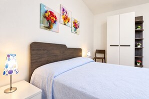 A bedroom with a bed, a nightstand, a lamp, a chair, a wardrobe, and wall art. - Casa Mina 154 (Torre Pali)