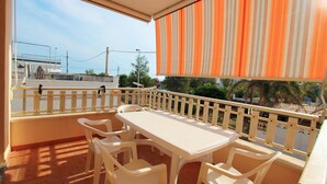 A balcony with a white table and chairs, a striped awning, and a view of buildings and trees.