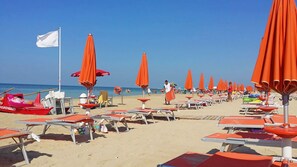A beach with rows of orange umbrellas and sun loungers, a lifeguard boat, and a clear blue sky. - Casa Mina 154 (Torre Pali)