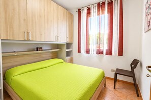 Een kamer met een bed, een houten garderobe, een stoel en een raam met gordijnen.