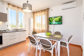 Una cuina moderna amb zona de menjador, un televisor fixat a la paret i una finestra amb cortines.
