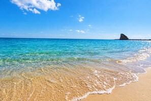 A beach with clear turquoise water, a sandy shore, and a rock formation in the distance. - Casa Mina 154 (Torre Pali)