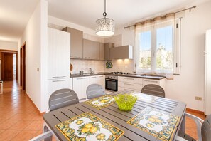 Een moderne keuken met een eethoek, met een tafel met decoratieve tafelkleed, een hanglamp en een raam met gordijnen.