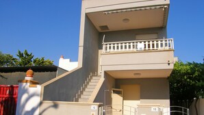 A two-story building with a balcony on the upper floor, a staircase leading to the entrance, and a gate with numbers 10 and 12.