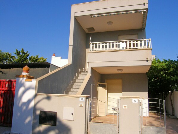 A two-story building with a balcony on the upper floor, a staircase leading to the entrance, and a red gate to the left. - Casa Mina 154 (Torre Pali)