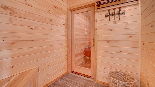 Una sauna de madera con puerta, un perchero con toallas y una cesta tejida.