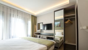 A modern hotel room with a large bed, a flat-screen TV, a mirror, a wardrobe, and a bedside table with a lamp. - Best Hotel Kadikoy (Istanbul)