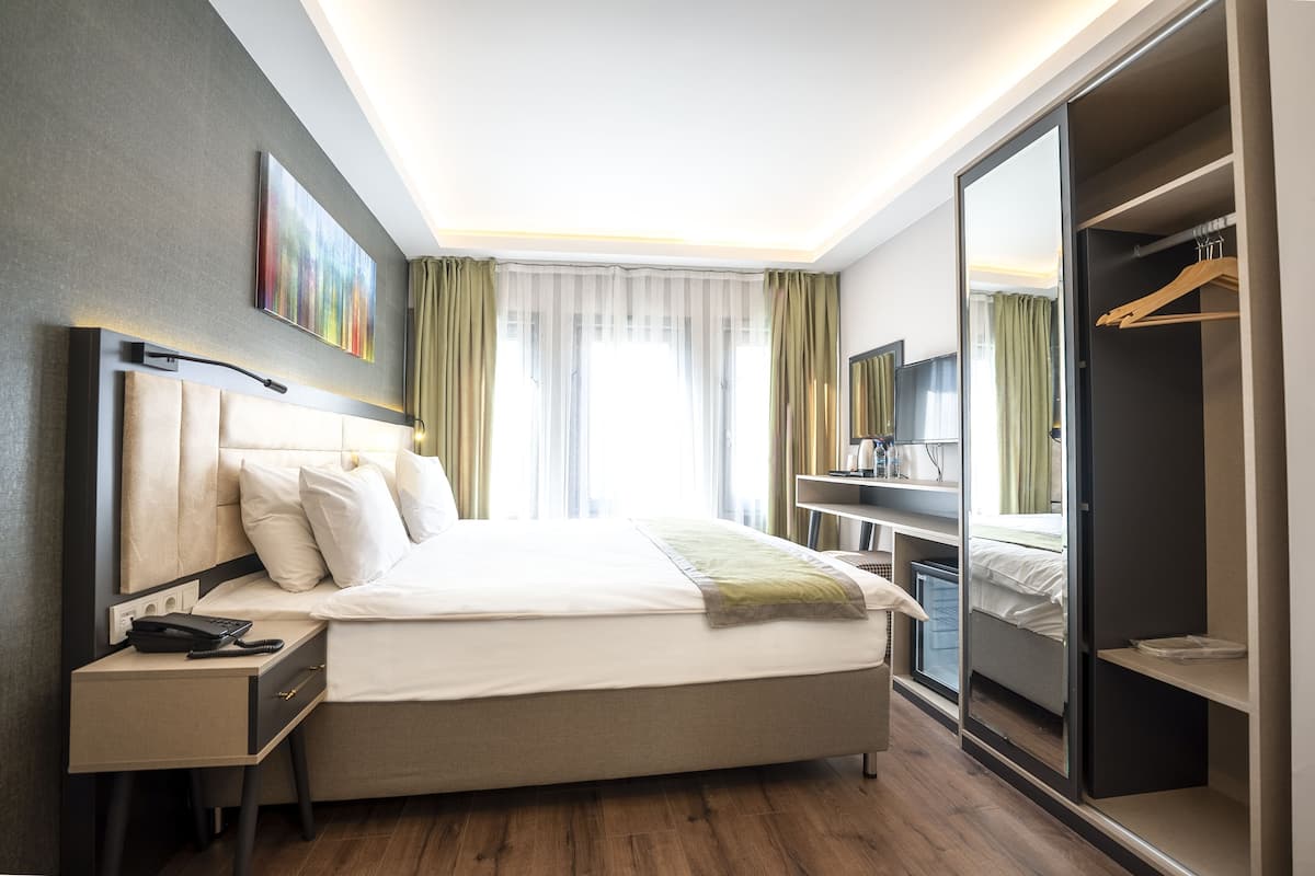 Ein modernes Hotelzimmer mit einem großen Bett, Nachttischen, einem Kleiderschrank und einem Schreibtisch mit Stuhl.