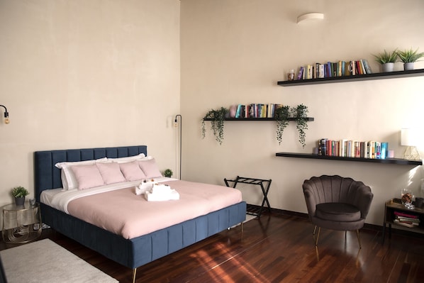A bedroom with a bed, bedside table, chair, and shelves with books and plants.