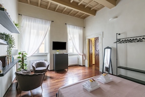 Quarto de hotel com uma cama, televisão, cômoda, cadeira e espelho.