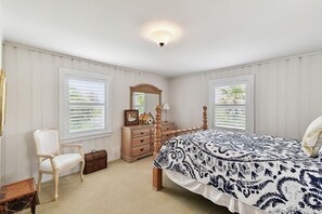 A bedroom with a bed, dresser, chair, and a window with blinds.