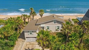 A beachfront property with a two-story house, a fenced yard, and palm trees.