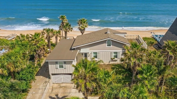 A beachfront property with a two-story house, a fenced yard, and palm trees.
