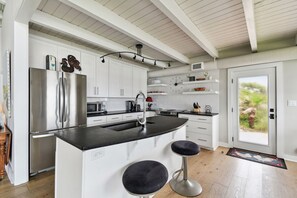 A modern kitchen with white cabinetry, a stainless steel refrigerator, a black countertop, and two bar stools.
