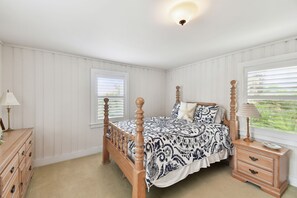 A bedroom with a four-poster bed, a wooden nightstand, a dresser, and a window with blinds.
