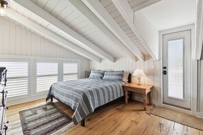 Ein Schlafzimmer mit einem Bett, einem Nachttisch, einer Lampe, einem Holzboden und einer Tür mit einem Fenster.