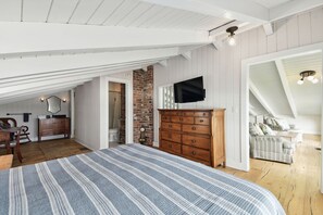 A bedroom with a large bed, wooden dresser, TV, and a loft area with a sofa.