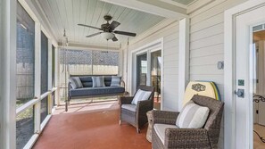 A covered porch with wicker furniture, a ceiling fan, and a surfboard.