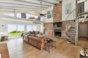 A spacious living room with a large leather sofa, a fireplace, and a high ceiling with exposed beams.