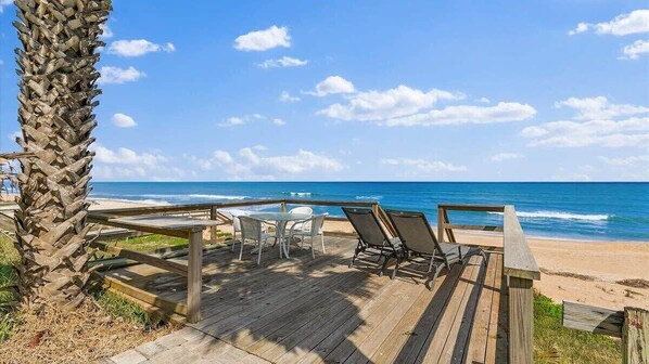A wooden deck with lounge chairs and a table overlooking the beach and ocean.