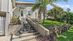A residential house with a concrete staircase leading to the front door, surrounded by a stone retaining wall and various plants.