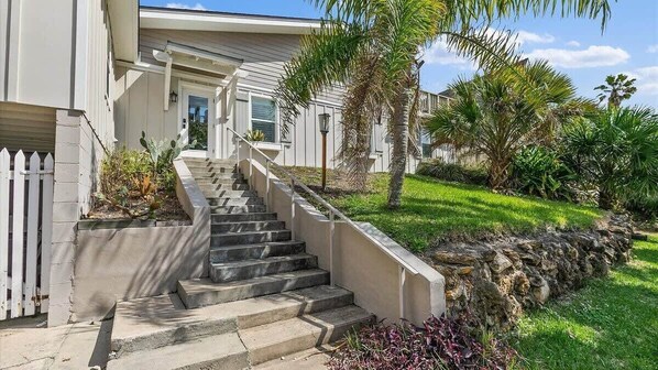 A residential property with a staircase leading to a front door, surrounded by a stone retaining wall and a variety of plants.