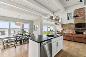 A spacious kitchen with a central island, a dining area with chairs, a built-in oven, and a large window overlooking a green landscape.