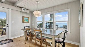 A dining area with a large window, wooden chairs, a table, and a pendant light.