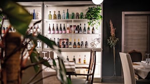 Una zona de bar con estantes llenos de botellas de licores, una mesa de comedor con sillas y una planta en maceta.