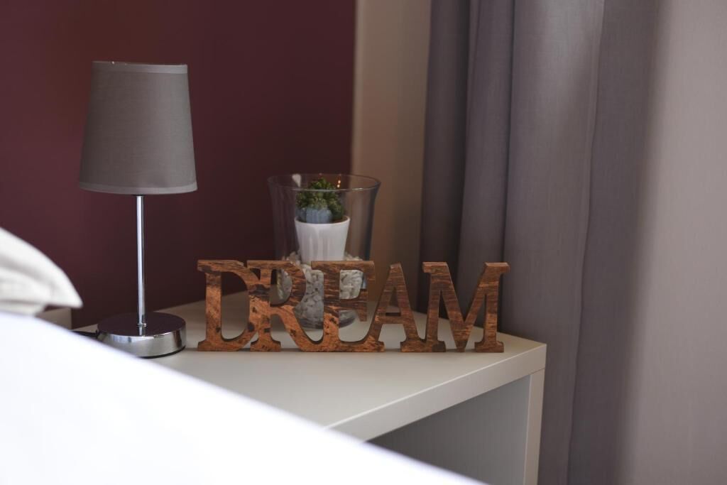 Ein Nachttisch mit Lampe, einer kleinen Topfpflanze und einem Holzschild mit der Aufschrift 'DREAM'.