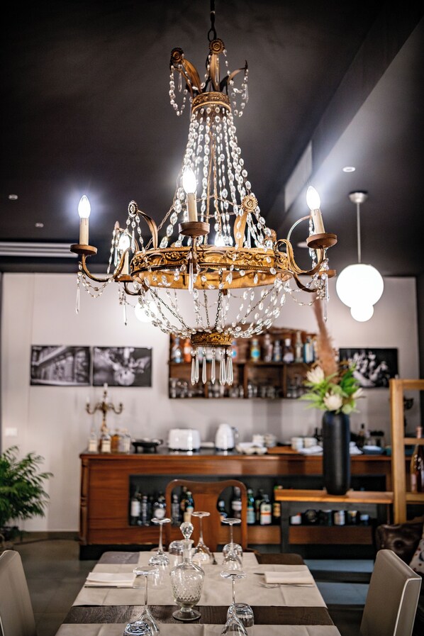Un lustre orné de nombreuses lampes rappelant des bougies, une table à manger en bois mise en scène avec de la verrerie, et un bar en arrière-plan.