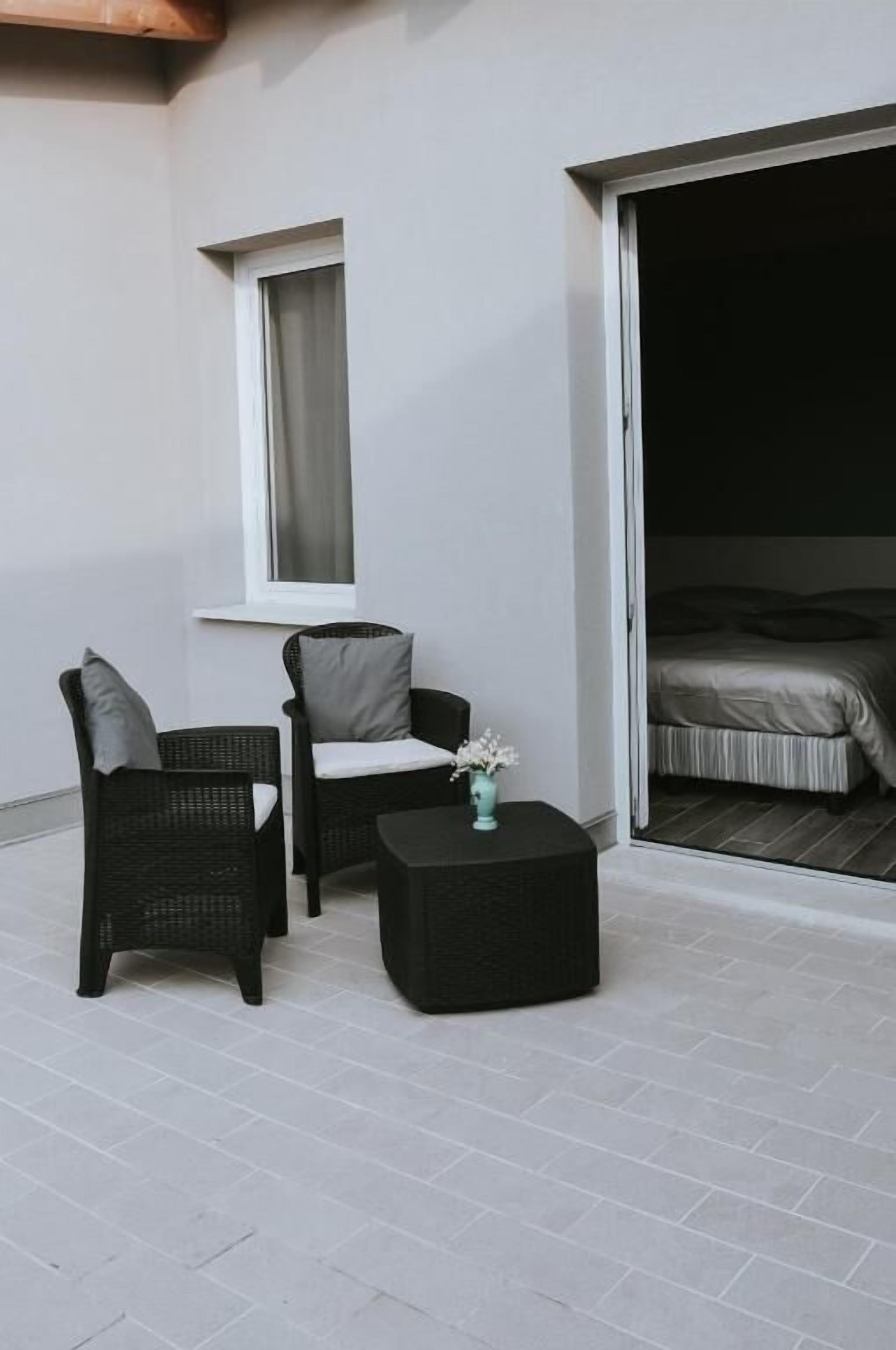 A balcony with wicker furniture, a small table with a vase, and a sliding door leading to a bedroom.