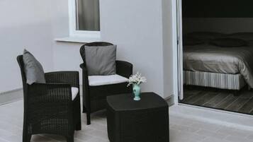 A balcony with wicker furniture, a small table with a vase, and a sliding door leading to a bedroom.
