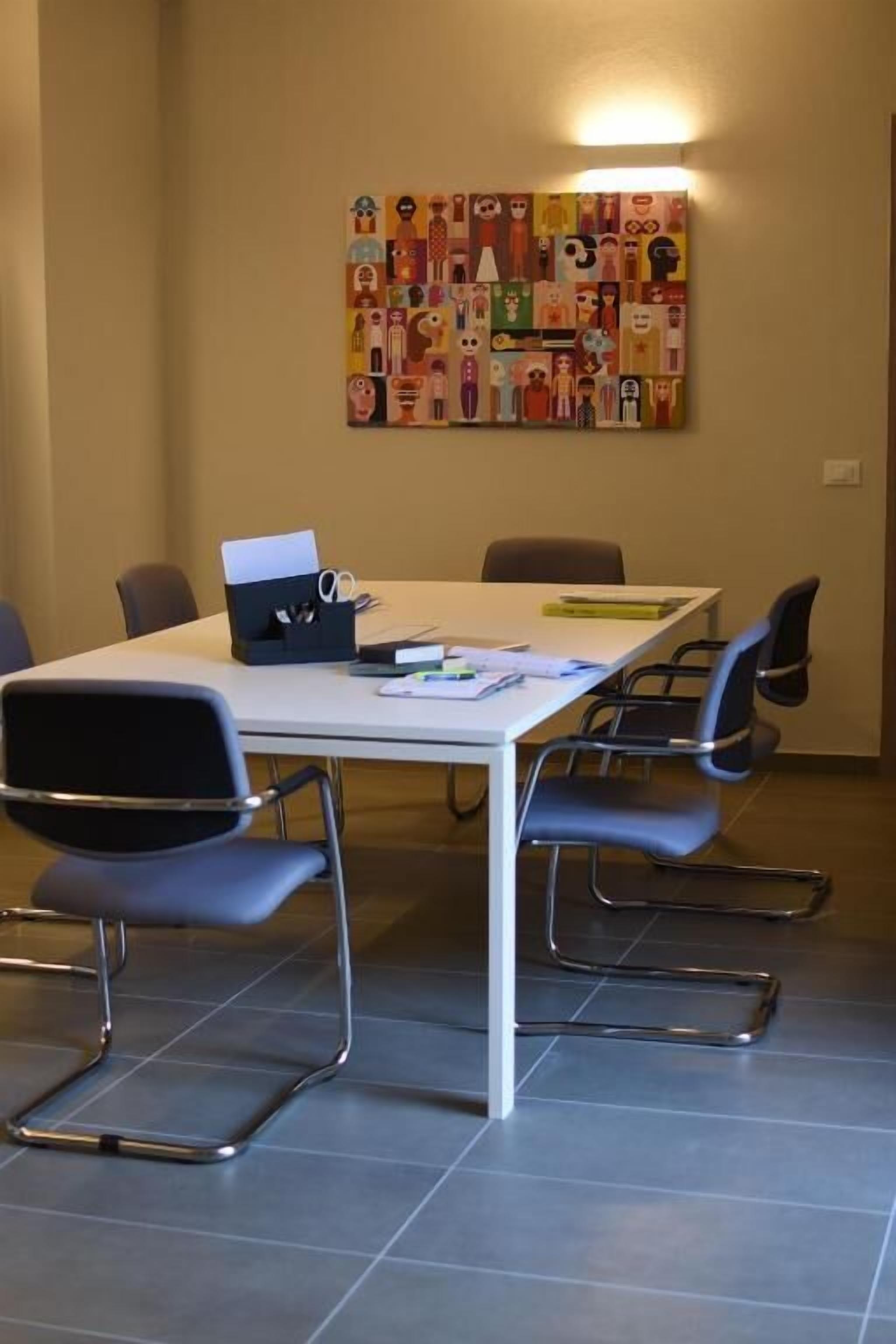 A conference room with a long table, six chairs, and a colorful abstract painting on the wall.