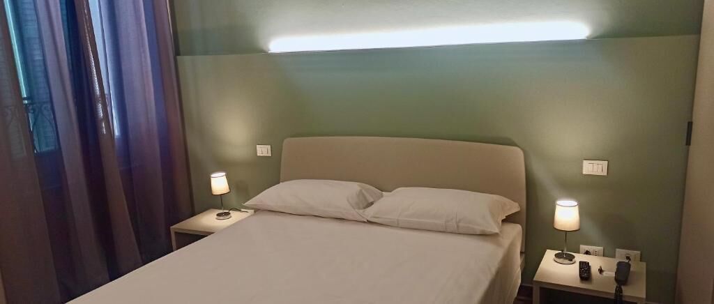 A hotel room with a bed, two bedside tables, a night lamp, and a wall-mounted light fixture.