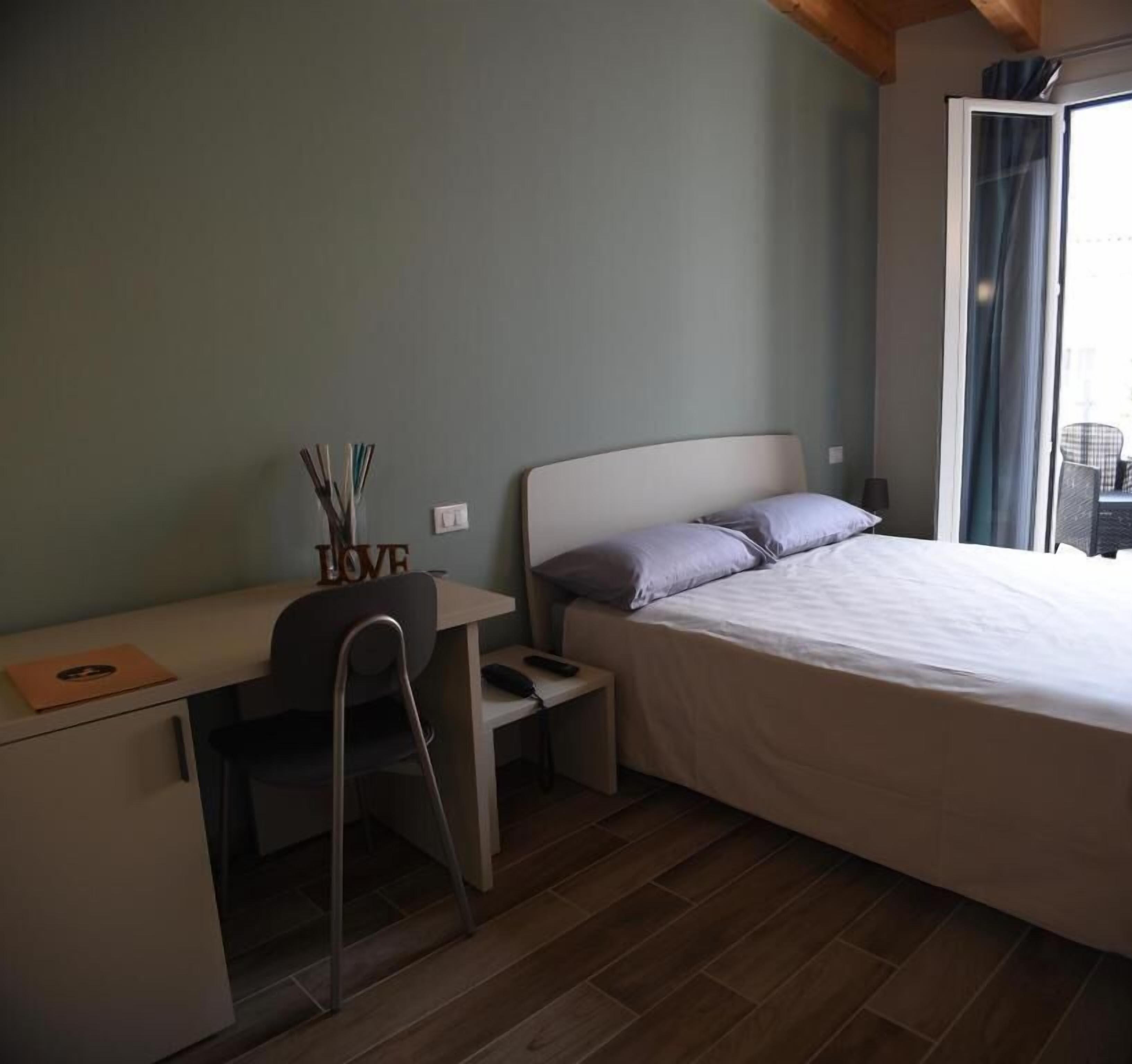 Un dormitorio con una cama, un escritorio y una silla. Hay una mesita de noche con una lámpara y un objeto decorativo en el escritorio.