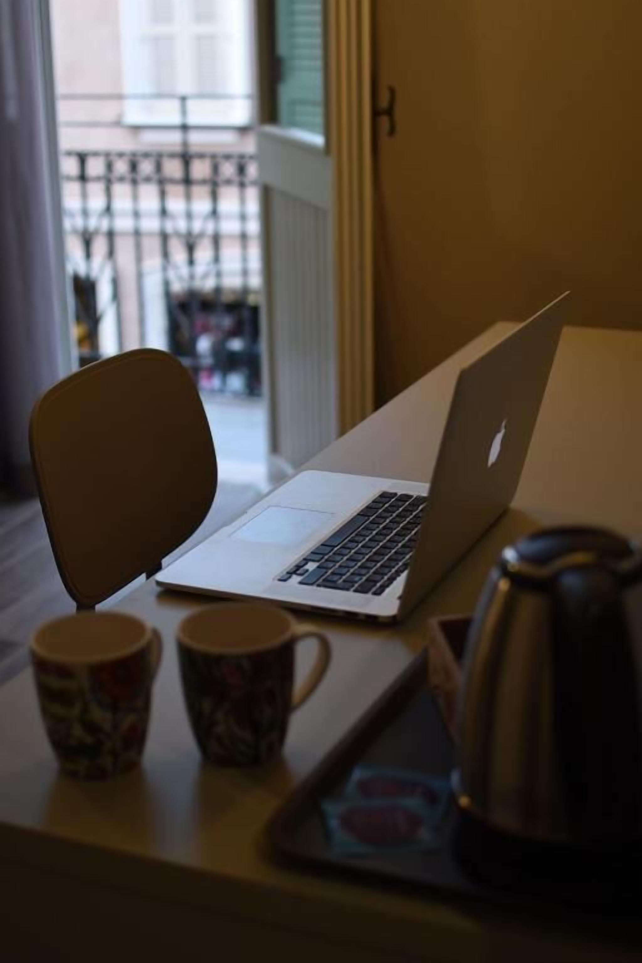 Un portàtil damunt d'un taulell amb dues tasses estampades i una cafetera.