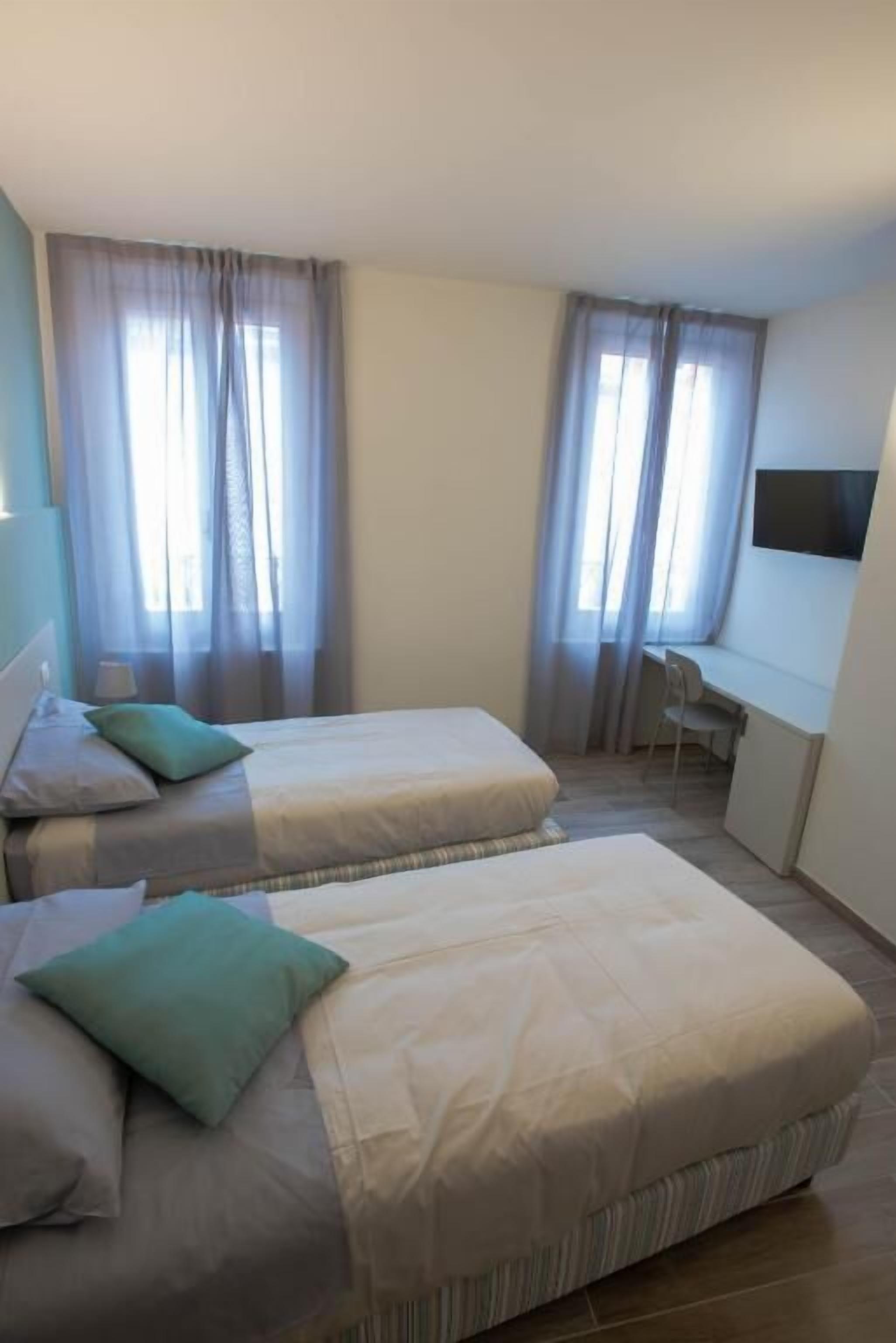A hotel room with two beds, a desk, and a TV.