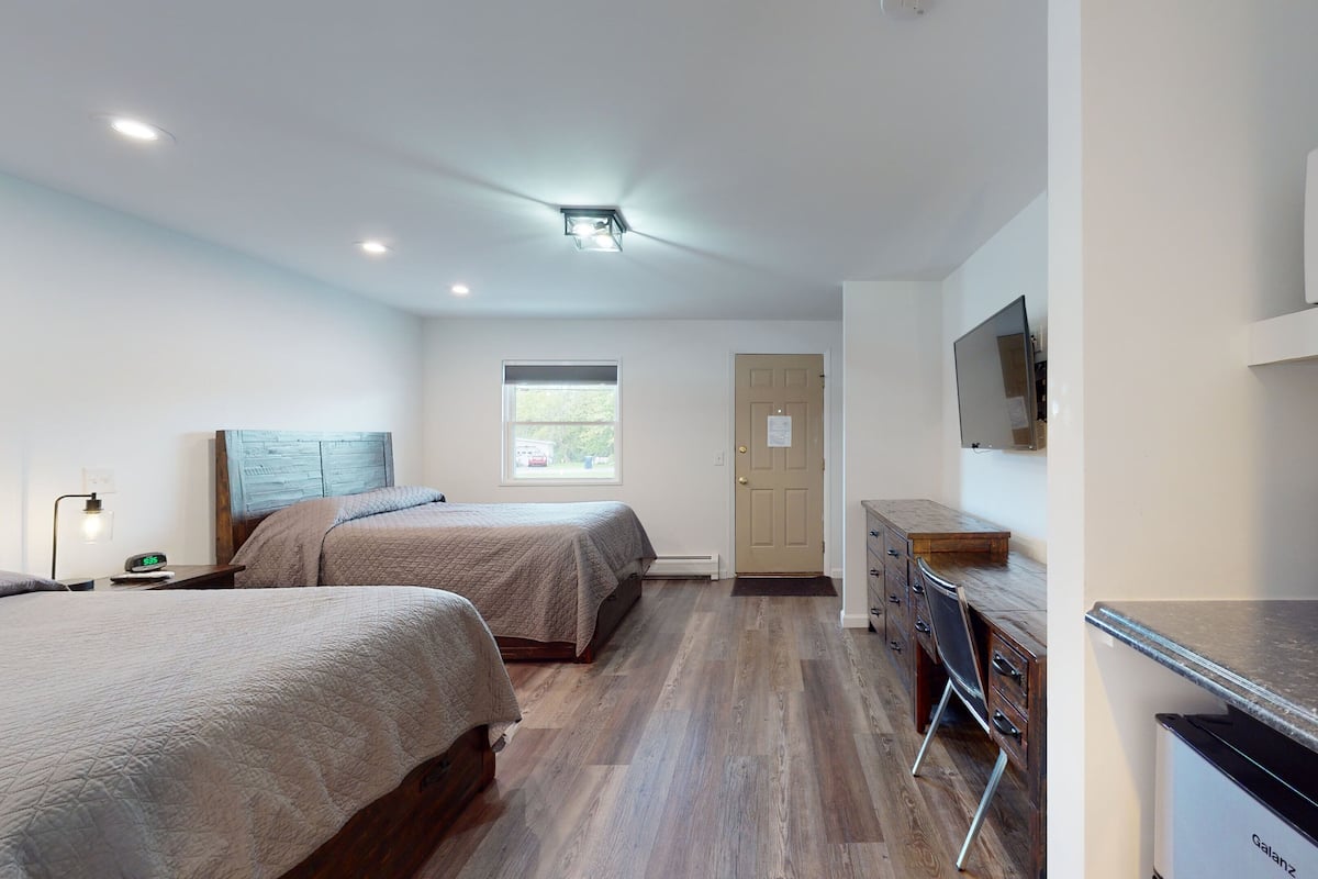 Habitación de hotel con dos camas, un escritorio, una cafetera y un televisor.