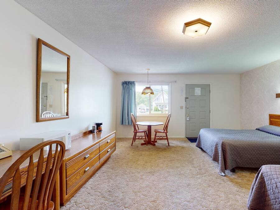 A hotel room with a bed, a desk with a telephone, a chair, a table with chairs, and a window with curtains.