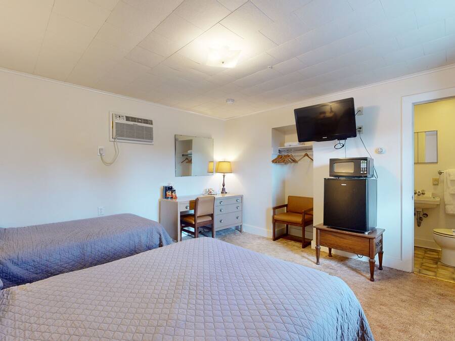 Habitación de hotel con dos camas, un escritorio con silla, televisor montado en la pared, microondas y baño visible a través de una puerta abierta.