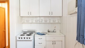 A compact kitchen with white cabinets, a stove, and a sink. - Siesta Motel (Colfax)